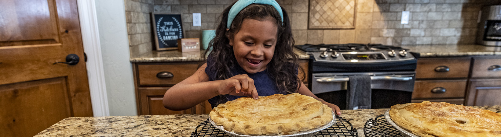 Little girl in the kitchen poking at a pie