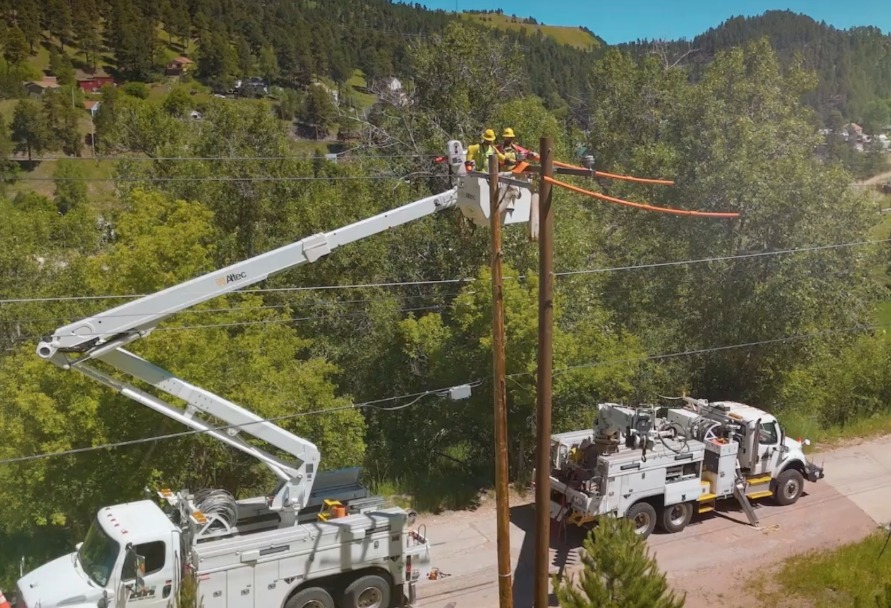Two lineman working at the top of a power pole with service trucks below