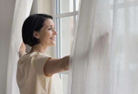 Woman opening window with white curtains