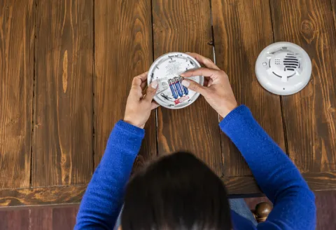 Overhead image of a woman replacing batteries in a smoke detector